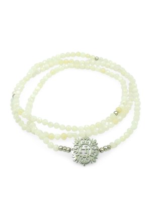 Bracelet blanc en perles avec de petits accents en argent et un charme décoratif en argent présentant un motif floral complexe et les lettres "H" et "T".