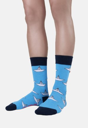 Blauwe sokken met een patroon van witte papieren boten, marineblauwe boorden en tenen. Zacht materiaal met een gladde textuur.