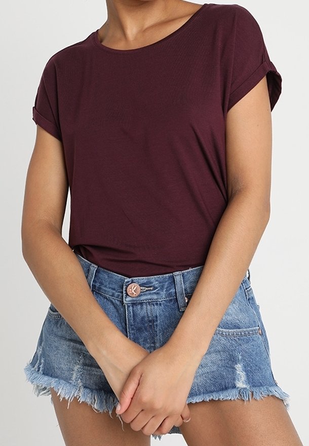 Personne portant une chemise bordeaux à manches courtes rentrée dans un short en jean taille haute à ourlet effiloché avec poches avant visibles.