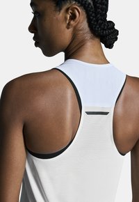 Top atlético blanco con acentos negros, que presenta un diseño de espaldas nadadora y tejido texturizado. Material suave y ligero, ideal para hacer ejercicio.