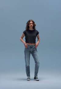 Must mustrilõikega t-särk, hele sinised teksad ja mustad-valged tossud. Modell seisab ühevärvilise helesinise tausta ees.