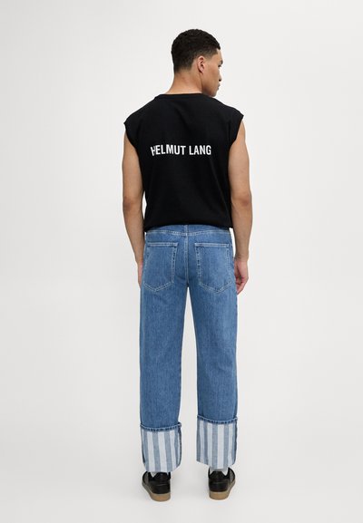 Camisa sin mangas negra con el logo "HELMUT LANG" en la parte posterior, acompañada de pantalones vaqueros azul claro con puños a rayas y dos bolsillos traseros.