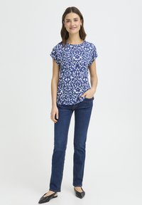 Sinise mustriga lühikeste varrukatega pluus ümmarguse kaelusega; kujundatud lillemustritega erinevates rohelistes ja sinistes toonides. Sobitatud tumedate teksapükstega.