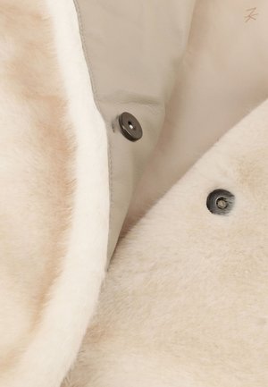 Helles beiges Lederjacken-Innenfutter mit weißem Lammfellfutter, ausgestattet mit schwarzen Druckknöpfen und weicher Textur.