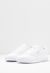 Bílé tenisky vyrobené z umělé kůže s kulatou špičkou, šněrovacím designem, texturovanou podešví a jemnými šedými logovými detaily.