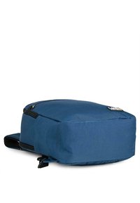 Mochila de tela azul con forma rectangular, cierre superior de cremallera y correas de hombro acolchadas. Presenta un parche con logo y costuras duraderas.