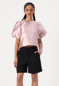 Lys rosa satin cropped topp med puff-ermer, kombinert med høy midje svarte shorts med rullet kant. Glatt tekstur, strukturert design.