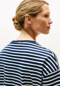 Granatowa i biała koszulka w paski o luźnym kroju, z krótkimi rękawami oraz subtelnym akcentem w kolorze czerwono-białym na dekolcie z tyłu. Materiał bawełniany.