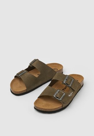 Braune Wildledersandalen mit zwei verstellbaren Riemen, silbernen Schnallen und einem Korkfußbett. Strukturierte schwarze Gummisohle. Markenzeichen auf dem Fußbett.