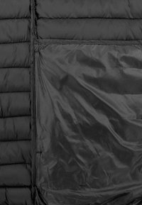 Schwarze Steppjacke mit einem ge quilteten Muster, glatter Textur und einer großen, mit Reißverschluss versehenen Tasche mit glänzender Oberfläche.