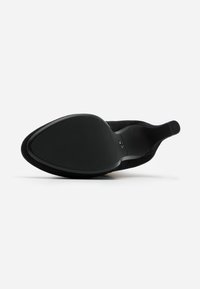 Scarpa nera con tacco alto e punta affusolata, realizzata in materiale scamosciato. Presenta una suola liscia e testurizzata e un design del tacco curvo.