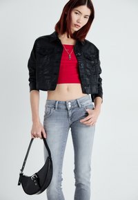 Jaqueta de ganga preta cropped, top vermelho cropped, jeans claros justos cinza claro com botões duplos, e uma bolsa preta com textura de crocodilo.