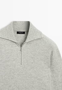 Grauer gerippter Pullover mit Reißverschluss am Halsausschnitt. Hergestellt aus weichem Stoff, mit lockerem Kragen und minimalistischem Design. Markenlabel sichtbar.