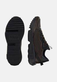 Baskets de sport marron avec un mélange de cuir souple et de textile, dotées d'une semelle en caoutchouc noir épaisse avec des rainures et des accents de marque.