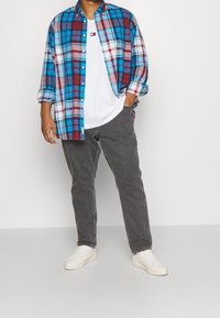 Camicia a quadri blu, rossa e bianca sopra una t-shirt bianca, abbinata a jeans grigi e sneakers bianche. Vestibilità casual, chiusura con bottoni.
