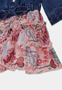 Haut en denim avec détail nœud et jupe en tulle rose à volants avec un imprimé style bande dessinée comprenant des mots comme "Happy," "Cool," et des cœurs.
