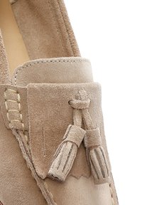 Mocassino in suede beige con dettaglio decorativo a nappina, accenti di cucitura e una finitura morbida e testurizzata.