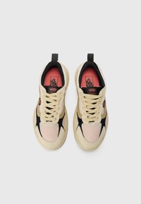 Beige og svarte sneakers med mesh- og semsket skinnmateriale, rund tå, polstret tunge, røde detaljer og fremtredende snørebånd.