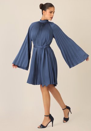 Blaues, plissiertes Kleid mit langen, ausgestellten Ärmeln und einer Taillenbindung. Es hat einen hohen Ausschnitt und eine glatte Textur, ergänzt durch hochhackige Sandalen.
