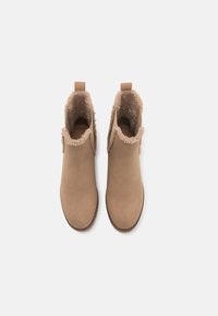 Hnědé kotníkové boots s hladkým semišovým povrchem, chlupatou podšívkou a texturovanou gumovou podrážkou. Obsahují poutko na zadní straně.