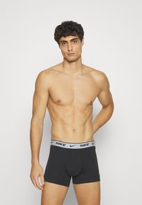 Schwarze Nike Boxer Shorts mit einem grauen Taillenbund, der das Nike-Logo zeigt. Der Stoff wirkt glatt und hat ein figurbetontes Design.