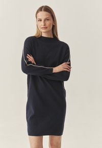 Navy Pulloverkleid mit langen Ärmeln, hohem Ausschnitt und kontrastierenden hellen Akzenten entlang der Ärmel. Weicher Stoff und lässige Passform.
