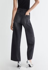 Jeans a gamba larga in denim scuro con due tasche posteriori e passanti per cintura. Texture liscia, vita alta e dettagli di cuciture a contrasto.