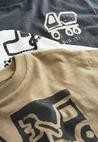 Two t-shirts stacked; one dark gray with a truck graphic, the second beige with abstract black designs. Both cotton, casual design.