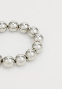 Bracelet en métal argenté composé de perles arrondies. Il présente une texture lisse avec une finition polie et de petites coutures décoratives entre les perles.
