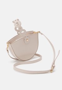 Round cream handbag made of faux leather, featuring a unique cut-out handle and a detachable shoulder strap with gold hardware accents.