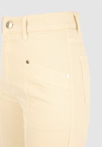 Beige denimbyxor med slim fit, framfickor med diagonala sömmar och en metallknapp för knäppning i midjan.