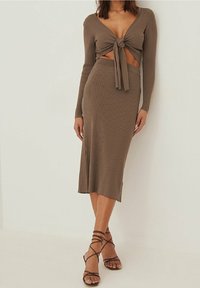 Ensemble deux pièces comprenant un crop top en tricot côtelé marron avec un nœud à l'avant et des manches longues, associé à une jupe mi-longue assortie.