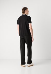 Schwarzes Polo-Shirt mit kurzen Ärmeln, ausgestattet mit weißen Akzenten am Kragen und den Ärmeln, kombiniert mit schwarzen Hosen und weißen Schuhen.