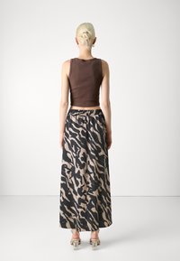 Top de tirantes ajustado marrón combinado con una falda larga de estampado que presenta un diseño abstracto en blanco y negro, cinturilla elástica y tacones transparentes de bloque.