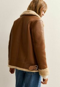 Giubbotto di pelle marrone con un morbido colletto e polsini in shearling beige, dotato di un dettaglio con fibbia in vita e una texture liscia.