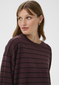Burgundy pruhovaný sveter s čiernymi horizontálnymi pruhmi, pletená textúra, široký okrúhly výstrih a dizajn s poklesnutými ramenami. Doplnkový s jemným rebrovaním.