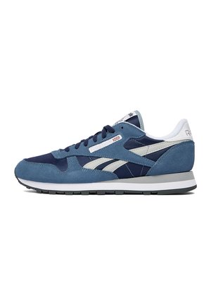 Blauer und marineblauer Reebok-Sneaker mit weißen Akzenten, Obermaterial aus Wildleder und Mesh, schwarze Schnürsenkel und eine graue und weiße Sohle, von der Seite gezeigt.