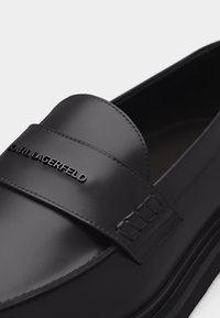 Μαύρο δερμάτινο μοκασίνι με φαρδιά λουρίδα και ανάγλυφο λογότυπο "KARL LAGERFELD" στο πάνω μέρος, με λεπτομερείς ραφές στο πλάι.