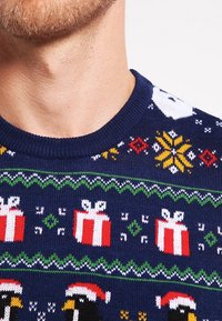 Marineblauwe trui met feestelijke patronen van sneeuwpoppen, cadeaus en pinguïns. Gemaakt van gebreide stof, met een geribde ronde halslijn en levendige kleuren.