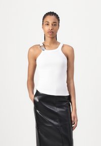 Witte geribbelde tanktop met een racerback-ontwerp en een zilveren accentband. Gecombineerd met een zwarte leren rok met een gladde textuur.