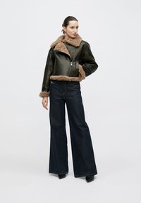 Giacca nera in pelle con fodera in shearling marrone, design corto, abbinata a jeans scuri a vita alta e stivali neri con tacco.