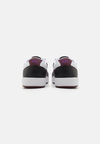 Black and white Vans sneakers with a maroon accent on the heel. Smooth leather upper and a thick white rubber sole. Simple, athletic design.