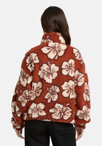 Pullover in fleece arancione bruciato con motivi floreali bianchi, colletto alto e vestibilità rilassata, caratterizzato da una superficie morbida e pelosa.