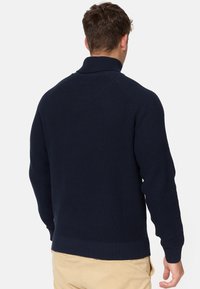 Granatowy sweter robiony na drutach z wysokim kołnierzem, prążkowanymi mankietami i dolnym brzegiem. Posiada fakturowany wzór oraz rękawy raglanowe dla większego komfortu.