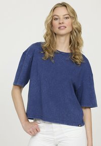 T-shirt cropped bleu en tissu doux et texturé, avec des manches courtes et un col rond. Présente des coutures visibles et une apparence légèrement usée.