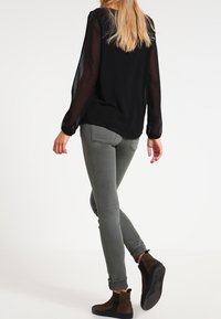 Czarna, przezroczysta bluzka z długim rękawem w połączeniu z szarymi, dopasowanymi dżinsami i brązowymi botkami za kostkę. Strój charakteryzuje się prostym fasonem z podwiniętymi mankietami.