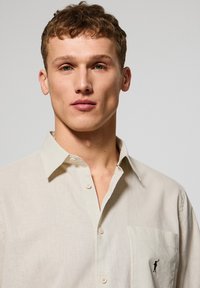 Crème-kleurig shirt van lichte stof, met een klassieke kraag, knopen aan de voorkant en een klein geborduurd ontwerp op de zak.