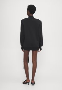 Sudadera negra de gran tamaño con cuello alto, que presenta mangas largas y puños de canalé. Textura suave con un ajuste relajado.