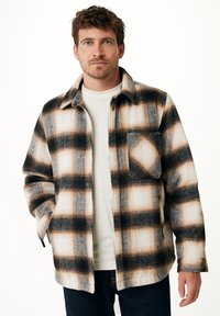 Camicia in flanella a quadri con colori nero, marrone e crema, presenta una chiusura con bottoni sul davanti e una tasca sul petto, mostrando una vestibilità rilassata e una piacevole texture.