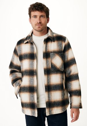 Plaid flannel shirt featuring black, brown, and cream colors, with a button-down front and a chest pocket, exhibiting a relaxed fit and texture.